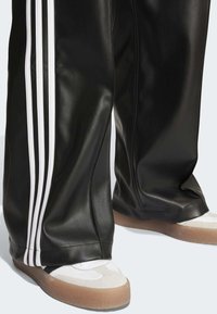 Svarta faux läderbyxor med tre vita sidostråk, matchade med vita och grå sneakers med en gummisula.