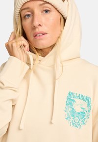 Huppari, jossa on turkoosi grafiikka, surffiteemalla ja kukkaaksentilla. Valmistettu pehmeästä kankaasta, jossa on ribbatut hihansuut.