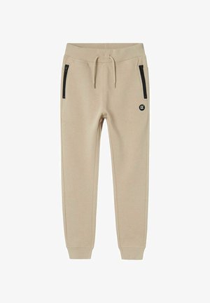 Beige Jogginghose aus weichem Material, mit schwarzen seitlichen Reißverschlusstaschen, einem gerippten Bund und einem kleinen Logo am linken Oberschenkel.