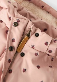 Rozā audums ar sarkanu un melnu kukaiņu rakstu, metāla pogas, rāvējslēdzis ar brūnu ādas cilpu un bežā mīkstā flīsa oderi.