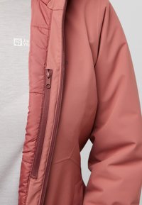 Roze geïsoleerde jas met een rits aan de voorkant, met een gladde textuur en een subtiel logo op de borst. Zichtbare zijzakken.