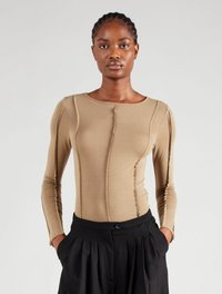 Beige Langarmoberteil mit tailliertem Design, betonten Nähten und rundem Ausschnitt. Kombiniert mit hochgeschnittenen schwarzen plissierten Hosen.