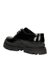 Scarpe in vernice nera con punta arrotondata, dotate di una suola in gomma nera spessa e robusta e dettagli con lacci.