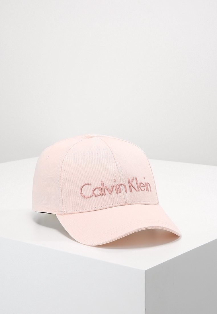 Casquette de baseball Calvin Klein rose clair avec une visière incurvée, présentée sur une surface blanche sur un fond uni.