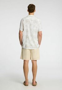 Kortærmet skjorte med let blomstermønster i hvid, parret med beige shorts, hvilket viser en afslappet pasform og glat tekstur.