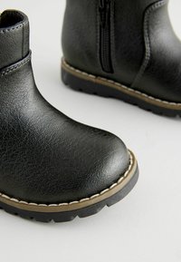 Schwarze Knöchelstiefel aus strukturiertem Synthetikleder, mit einem seitlichen Reißverschluss, einer dicken, geriffelten Sohle und kontrastierenden Nähten.