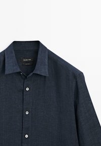 Dark blue long-sleeve button-up shirt with pointed collar, visible buttons, and stitched seams on a white background.