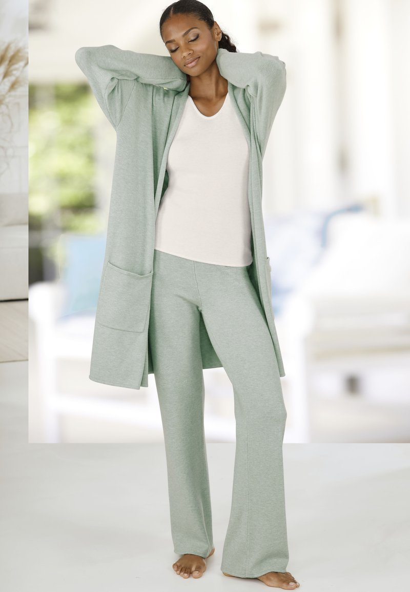 Vihreä pitkä neuletakki, yhteensopiva tiukka toppi ja pehmeästä kankaasta valmistetut levenevät housut. Ominaisuuksiin kuuluu tilava etutasku ja rento istuvuus.