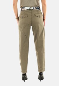 Pantalon en coton vert olive à jambe droite, doté de deux poches arrière et accompagné d'une ceinture à motif noir et blanc. Porté avec des escarpins noirs.