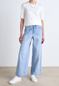 White short-sleeve shirt with a round neckline, paired with light blue wide-leg jeans, complemented by white sneakers. Simple chain necklace.