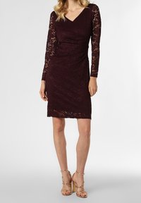 Burgundy spetsklänning med långa ärmar, V-ringning, figursydd silhuett och scalloped fåll. Höjd med ett texturerat blommönster.