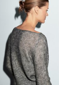Grå, løst strikket sweater med åben rygdesign, der har et tekstureret, blødt stof—der fremhæver en oversized pasform og et afslappet udseende.