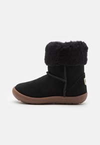 Bottines en daim noir avec un revers en fourrure de mouton, semelle en caoutchouc plate et laçage décoratif. Présente une étiquette logo à l'arrière.