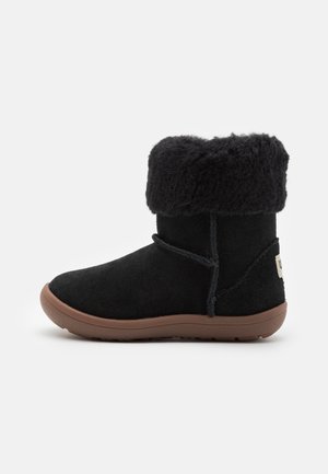Bottines en daim noir avec un revers en fourrure de mouton, semelle en caoutchouc plate et laçage décoratif. Présente une étiquette logo à l'arrière.