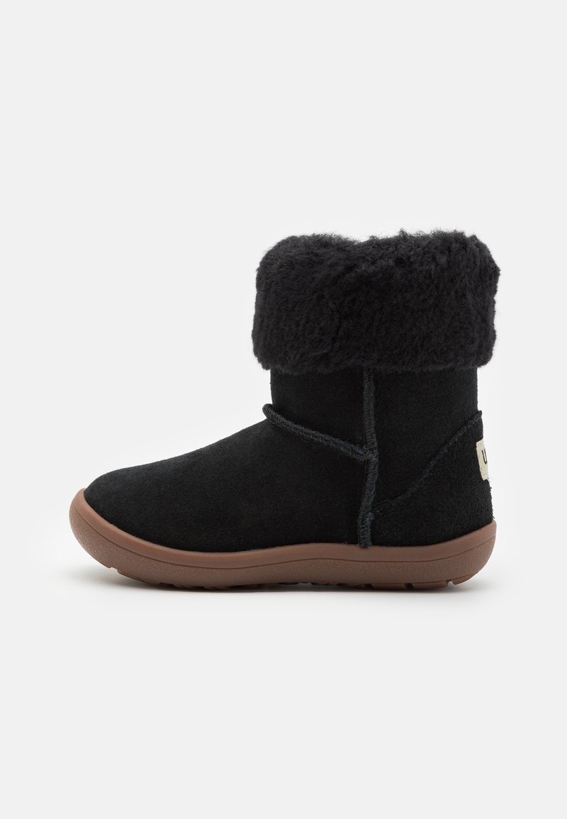 Bottines en daim noir avec un revers en fourrure de mouton, semelle en caoutchouc plate et laçage décoratif. Présente une étiquette logo à l'arrière.
