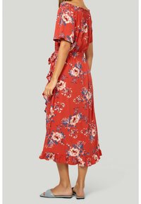 Vestido maxi rojo con flores, de mangas cortas, escote Bardot, cinturón en la cintura y dobladillo con volantes. Presenta patrones florales en crema y azul.