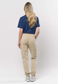 Avslappnad outfit med en marinblå kortärmad skjorta och beigea joggers med elastiska muddar, kombinerat med ljusgrå sneakers.