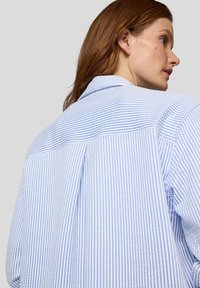 Blau-weißer, vertikal gestreifter Hemd mit Kragen, sichtbaren Nähdetails und lockerem Schnitt. Verfügt über einen Rückenpasse und eine weiche Textur.