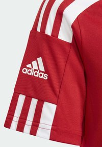 Rød sportstrøje med hvide detaljer, der har tre hvide striber på skuldrene og en broderet hvid Adidas-logo på ærmet.