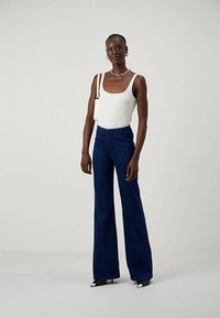 Woman wearing white sleeveless top, dark blue high-waisted wide-leg pants, black and white pointed heels, and white shoulder bag.