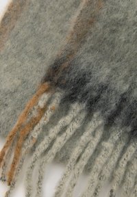 Vlnený šál so soft, jemnou textúrou. Predovšetkým šedý s oranžovými a čiernymi akcentmi. Má strapce na okrajoch pre dodatočný detail.