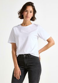 Vit t-shirt med kort ärm och klassisk rund halsringning. Bärs med svarta högmidjade jeans. Enkelt, avslappnat design. Slät bomullstextur.