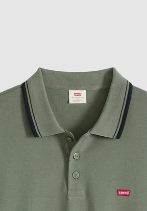 Olivengrøn polo lavet af tekstureret stof, med klassisk krave, to knapper og marineblå striber langs kravekanten. Rødt logo-patch.