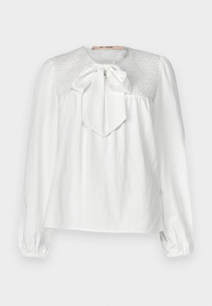 Blusa blanca con escote redondo, lazo en el cuello y detalles de fruncido en la yugo. Mangas largas y recogidas con puños elásticos.