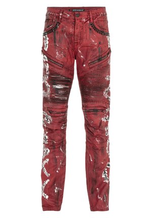 Rote Jeans aus Denim mit glänzender Oberfläche, die abgenutzte Muster, Reißverschluss-Taschen und Nieten-Details am Bund aufweisen.