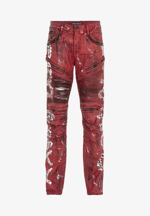 Rote Jeans aus Denim mit glänzender Oberfläche, die abgenutzte Muster, Reißverschluss-Taschen und Nieten-Details am Bund aufweisen.