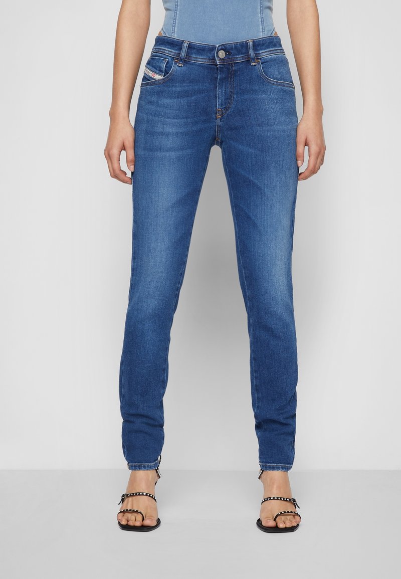 Jean en denim bleu avec une coupe slim, une taille mi-haute, des poches avant et un léger dégradé. Associé à des sandales noires à lanières.