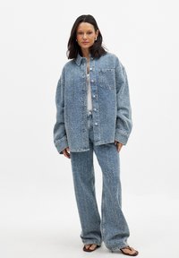 Blue denim jacket and matching pants, featuring a relaxed fit, wide legs, textured fabric, and front pockets. Open button-up style.