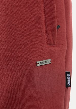 Rode sweatshirt met een zachte textuur, voorzien van een zilveren "SMILODOX"-label en een zwart zijlabel. Heeft een opvallende zakdetail.