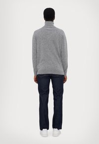 Grijze coltrui met een getailleerd design, ribgebreide manchetten, gecombineerd met donkerdenim jeans en witte sneakers, gezien vanaf de achterkant.