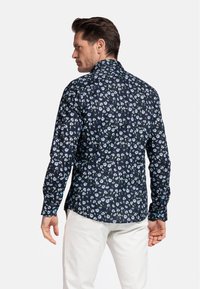 Chemise florale marine à manches longues, avec un petit motif de fleurs blanches et bleues. Coupe ajustée avec un col classique et des poignets à boutons.
