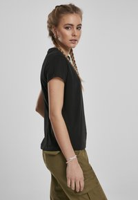 T-shirt noir à manches courtes en tissu doux, affichant une coupe décontractée. Porté avec un pantalon cargo vert olive et un bracelet léger.