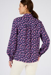 Blusa a maniche lunghe di colore navy con un motivo a foglie in rosa e bianco. Tessuto morbido con una leggera lucentezza, vestibilità comoda e polsini con bottoni.