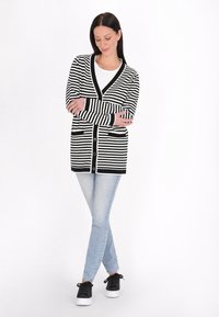 Czarny i biały kardigan w paski z długimi rękawami, dekoltem w serek, guzikami z przodu i kieszeniami, połączony z jasnoniebieskimi dżinsami i czarnymi butami.