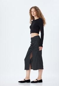 Un haut noir à manches longues et court associé à une jupe noire à pois avec une fente sur le côté. La jupe est de longueur mi-mollet et possède une texture lisse.