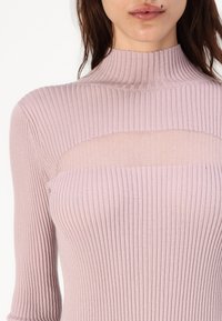 Zribovaná dlouhá rukávová blůza v jemné růžové barvě, s vysokým límcem a průhledným panelem přes hruď; přiléhavá textura s vertikálními pruhy.