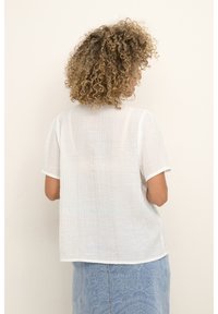 Haut blanc léger et texturé à manches courtes avec une coupe décontractée et un col rond, associé à une jupe en jean bleue à motif paisley.