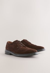 Chaussures habillées en daim marron avec un design classique à lacets, présentant des accents brogués et une semelle en caoutchouc noire. Forme simple et élégante.