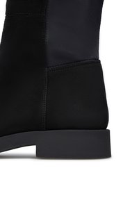 Stivale alla caviglia nero con esterno in suede morbido, suola in gomma e un design elegante con un pannello testurizzato a contrasto.