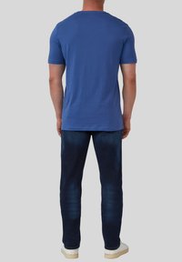 Blauwe katoenen t-shirt met korte mouwen, ronde halslijn en een relaxte pasvorm, gecombineerd met donkere spijkerbroek en witte sneakers.