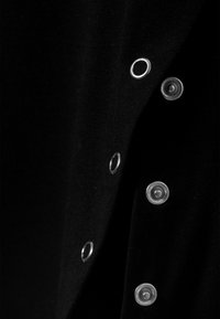 Primo piano di tessuto nero con bottoni automatici in argento e occhielli in argento abbinati lungo il bordo.