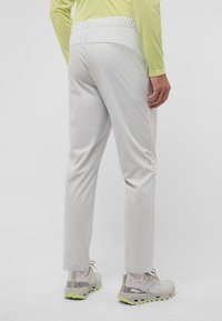 Helle graue Sporthosen mit elastischem Bund, schmal zulaufenden Beinen und kleinen Belüftungslöchern an den Seiten, kombiniert mit hellen Sneakers.