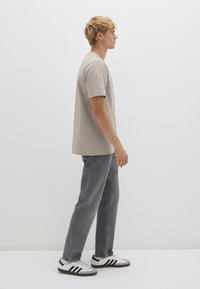 Gray striped t-shirt, relaxed fit, paired with faded gray jeans and white sneakers featuring black stripes. Model shown in profile.