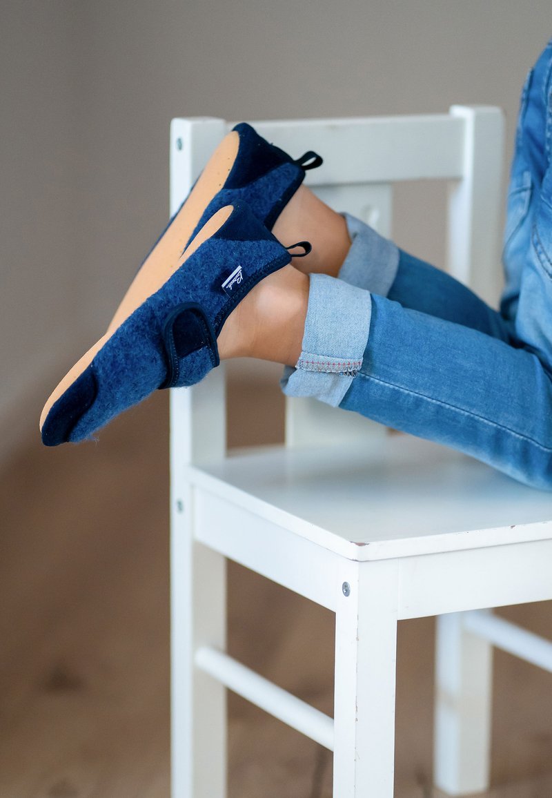 Marineblauwe instappers van gestructureerde stof met uitsparingen aan de zijkanten en een tan rubberen zool, voorzien van verstelbare straps en een klein logo.