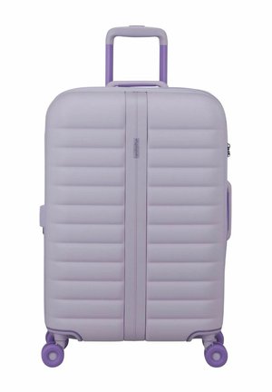 Valise rigide mauve avec des rainures horizontales, poignée télescopique violette, poignées latérales et quatre roues pivotantes violettes.
