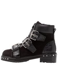 Botas tobilleras negras con una combinación de ante y cuero pulido, que presentan múltiples hebillas decorativas, acentos texturizados y detalles de tachuelas.